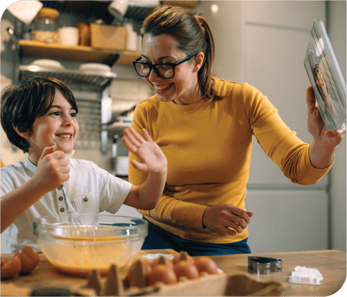 Parent and child smiling and baking together in a kitchen while video chatting on a tablet. Parent and child smiling and baking together in a kitchen while video chatting on a tablet.