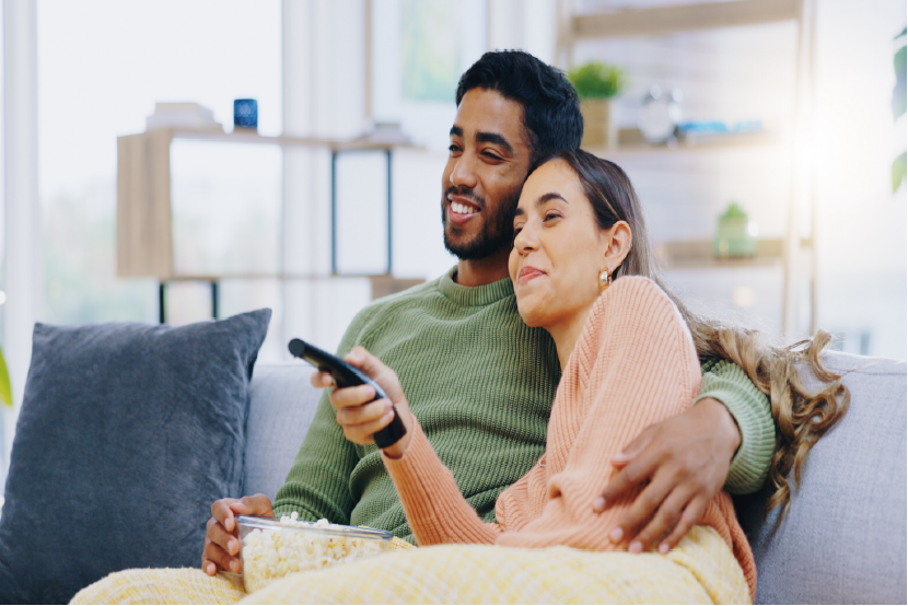 Couple smiling enjoying popcorn on a couch while watching tv. Couple smiling enjoying popcorn on a couch while watching tv.