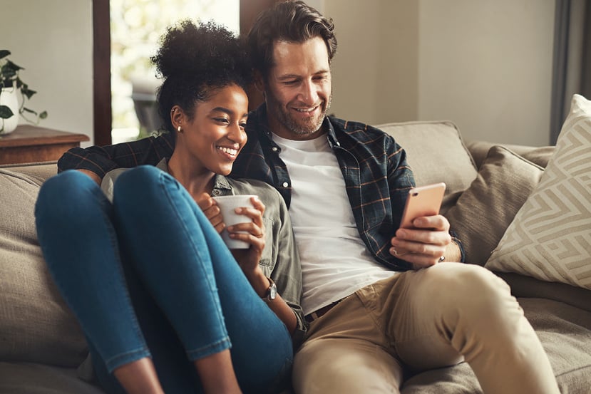 Couple cozied up on the couch looking at a mobile device. Couple cozied up on the couch looking at a mobile device.