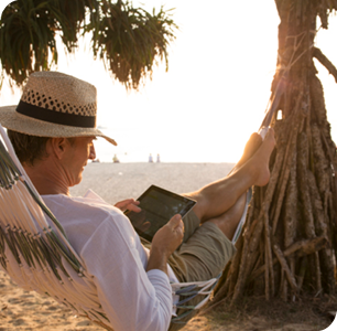 Man in hammock on a beach on his tablet.