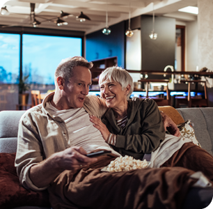 Older couple on couch enjoying popcorn watching tv.